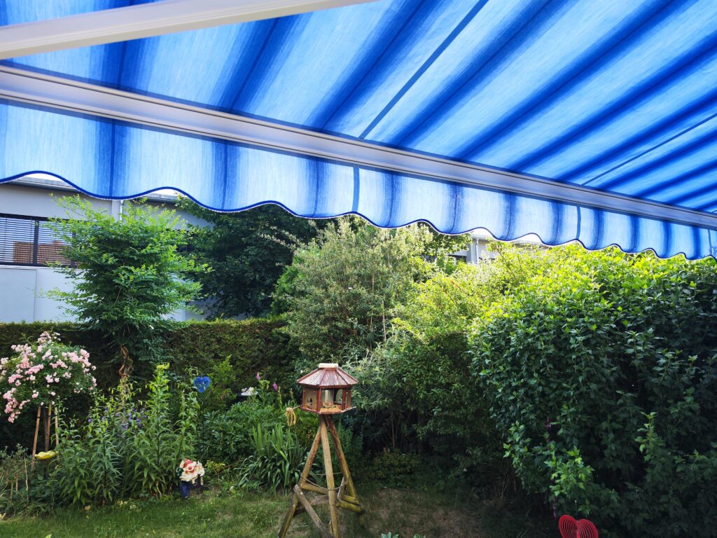Fachgerechtes Einziehen des neuen Markisentuches mit blauen Streifen in die Tuchwelle.