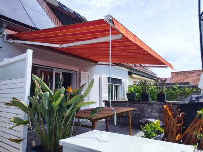 Ein neues Markisentuch mit rotem Multistreifen sorgt auf einer Terrasse in Haunstetten für Schatten.