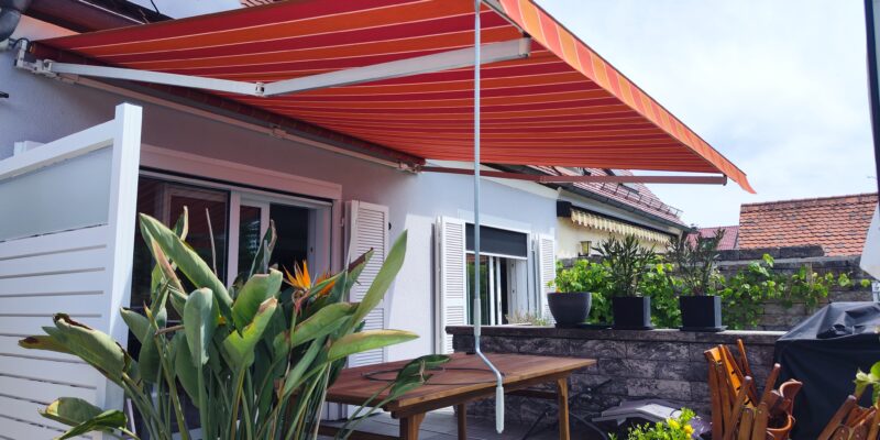 Ein neues Markisentuch mit rotem Multistreifen sorgt auf einer Terrasse in Haunstetten für Schatten.